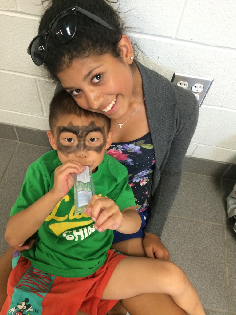 Smiling counselor and camper with Batman face paint eating a freezie.